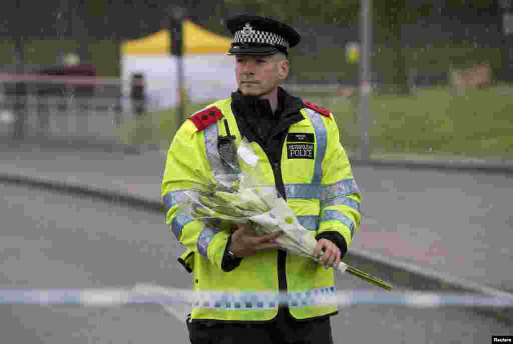 A police officer carries flowers near the scene of the killing of a British soldier in Woolwich, southeast London. The soldier was hacked to death on May 22, 2013, by two men shouting Islamic slogans in a south London street. 