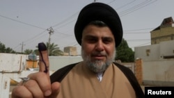 Ulama Shiah yang populis, Moqtada al-Sadr menunjukkan jarinya yang sudah dicelupkan tinta seusai memberikan suara di sebuah TPS di Najaf, Irak, 12 Mei 2018. (Foto: dok). 