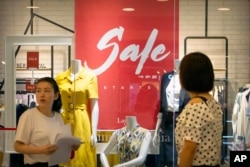 People walk past a store advertising a sale in a shopping mall in Beijing, Aug. 2, 2019.