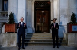 Britain's Foreign Secretary Dominic Raab, left, and Chancellor Rishi Sunak clap outside the Foreign and Commonwealth Office during a Clap for Carers NHS initiative to applaud NHS workers fighting the coronavirus pandemic in London, April 9, 2020.