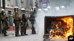 A fire burns as riot police look on during clashes with activists protesting German Chancellor Angela Merkel's visit in Athens, Greece, Oct. 9, 2012. 