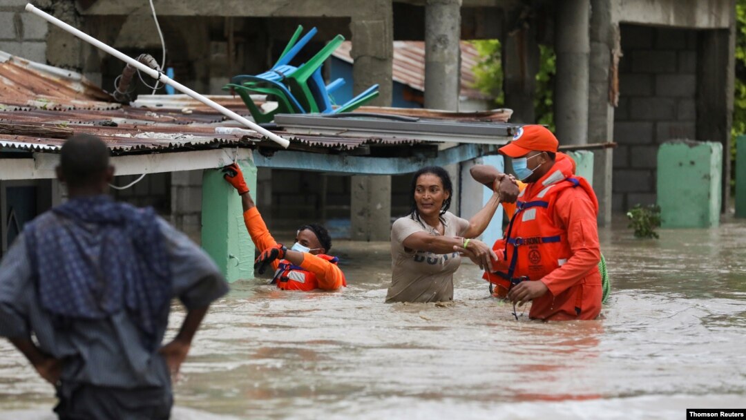 Miembros de la Defensa Civil ayudan a varias personas a salir de zonas inundadas por la tormenta Laura en Azua, Republica Dominicana.