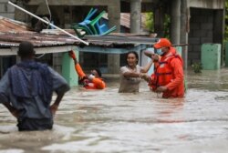 Miembros de la Defensa Civil ayudan a una mujer en una calle inundada tras el paso de la Tormenta Laura, en Azua, República Dominicana.