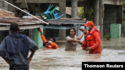 Miembros de la Defensa Civil ayudan a varias personas a salir de zonas inundadas por la tormenta Laura en Azua, Republica Dominicana.