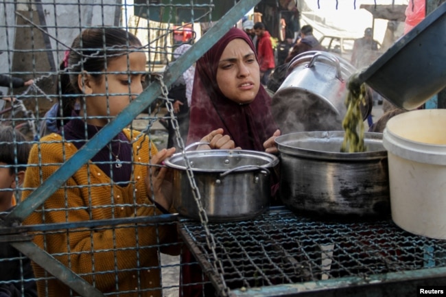 Palestinians wait to receive a free meal comprising Khobiza, a wild leafy vegetable, during the holy month of Ramadan, amid the ongoing conflict between Israel and Hamas, in Jabalia in the northern Gaza Strip, March 22, 2024. (REUTERS/Mahmoud Issa)
