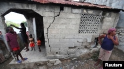 Des gens se tiennent devant leur maison après qu'elle a été endommagée par un tremblement de terre, qui a frappé le nord d'Haïti tard samedi, à Port-de-Paix, en Haïti, le 8 octobre 2018.