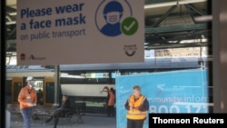 People are seen on a train platform below a sign encouraging the use of protective face masks in the city center in Sydney, Australia, Aug. 28, 2020.
