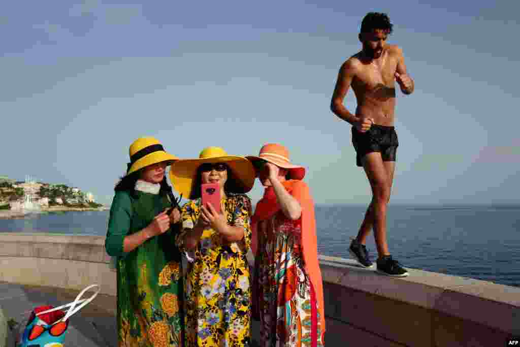 A man walks by as tourists take selfies on the French Riviera city of Nice, June 24, 2019, as temperatures soar to 33°C (94°F).