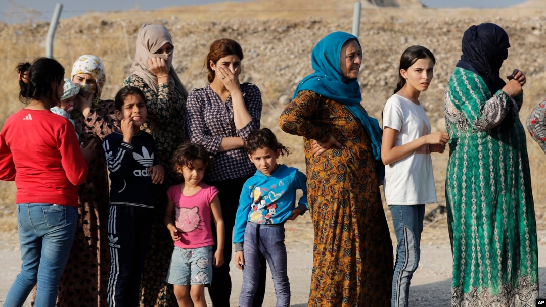 Syrian women who were displaced by the Turkish military operation in northeastern Syria line up to receive aid and food supplies, at the Bardarash refugee camp, north of Mosul, Iraq, Thursday, Oct. 17, 2019.