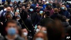 FILE - Shoppers wearing face coverings walk down Oxford Street, Europe's busiest shopping street, in London, Dec. 23, 2021. Scientists are seeing signals that COVID-19′s omicron wave may have peaked in Britain.