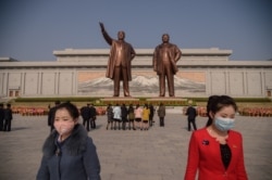 مجسمه‌های کیم جونگ ایل و پدرش کیم ایل سونگ، و دو هوادار با ماسک ضدویروس کرونا، که از بازدید مجسمه‌ها باز می‌گردند - عکس