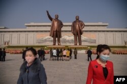 مجسمه‌های کیم جونگ ایل و پدرش کیم ایل سونگ، و دو هوادار با ماسک ضدویروس کرونا، که از بازدید مجسمه‌ها باز می‌گردند - عکس