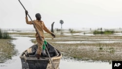 FILE - John Gafabusa, custodian of the Mutyona natural sacred site near Buliisa, Uganda, points at a water covered sacred site on Lake Albert at the Karakaba landing site, on Aug. 3, 2023.