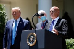 President Donald Trump, left, listens as Moncef Slaoui, a former GlaxoSmithKline executive, speaks about the coronavirus in the Rose Garden of the White House, May 15, 2020, in Washington.