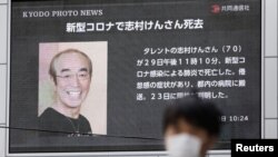 A man wearing a protective face mask walks past in front of a huge screen reporting death of Japanese comedian Ken Shimura, who died after being infected with the new coronavirus, in Osaka, western Japan March 30, 2020.