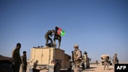 Seorang Marinir AS memperhatikan saat tentara Angkatan Bersenjata Afghanitan menaikkan bendera Afghanistan saat latihan militer di Kamp Militer Shorab, di Provinsi Helmand, 28 Agustus 2017. (Foto: Wakil Kohsar/AFP)