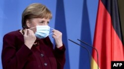 German Chancellor Angela Merkel takes her face mask off as she arrives to a press conference at the chancellery in Berlin, Germany, on March 19, 2021.