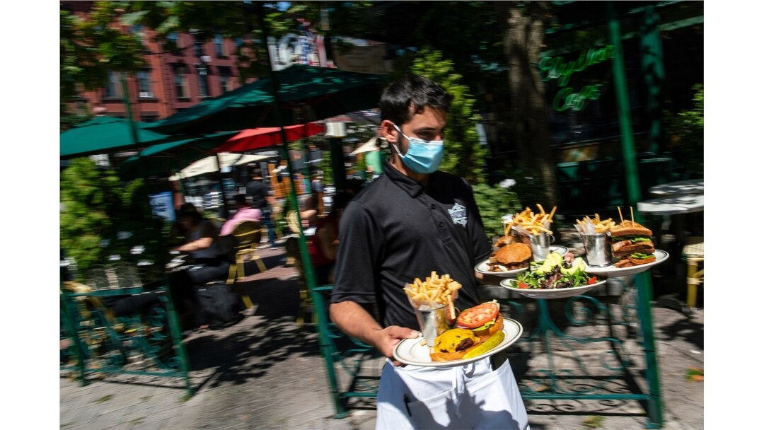 A waiter in a face mask delivers food to the tables outside of a local restaurant during lunch in Hoboken, N.J., Sept. 4, 2020.