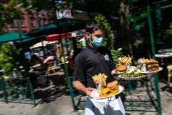 A waiter in a face mask delivers food to the tables outside of a local restaurant during lunch in Hoboken, N.J., Sept. 4, 2020.