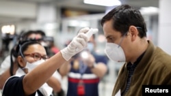 Un pasajero es revisado con un escáner térmico por un trabajador de salud pública en el aeropuerto internacional Óscar Romero y Galdamez, en El Salvador, el 12 de marzo de 2020
