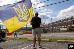 Maxim Trushin, oriundo de Ucrania, ondea una bandera antes de que la caravana del presidente de Ucrania, Volodymyr Zelenskyy, llegue a la planta de municiones del ejército de Scranton, en Scranton, el domingo 22 de septiembre de 2024. (Foto AP/Laurence Kesterson)