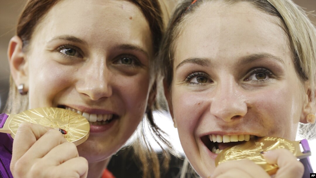 Atlet Jerman Kristina Vogel (kanan) dan teman satu tim Miriam Welte menggigit medali emas yang dimenangkan dalam nomor sepeda trek cepat putri di London. (Foto: AP)