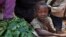 A young boy eats some of the leaves that a market-seller, left, is chopping up for sale at the market in the Bimbo neighborhood of the capital Bangui, Central African Republic, January 1, 2013. 