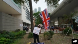 一位民主派支持者于2021年4月16日在香港法庭外挥舞英国国旗。包括82岁的香港民主党创建人李柱铭和支持民主的媒体大亨黎智英在内的七位香港主要的民主派人士因参与2019年8月的一次集会，被控参与未经授权的集结罪名。周五法官对七人做出宣判。