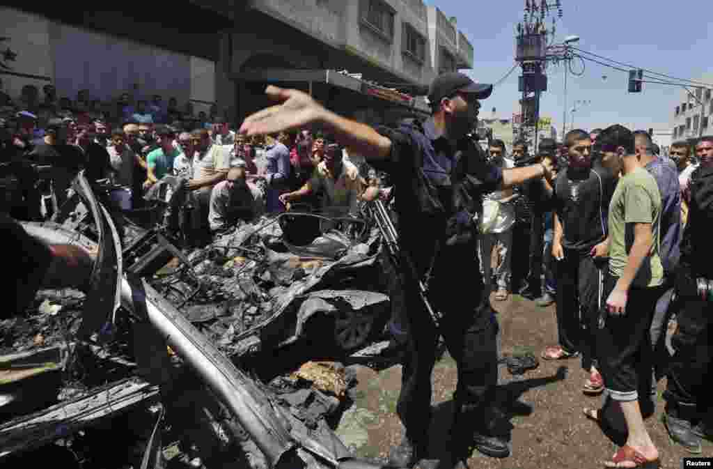 Polisi di tengah warga Palestina yang melihat-lihat bangkai mobil yang menurut polisi merupakan sasaran dalam serangan udara Israel di kota Gaza (8/7).