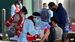 In this Jan. 13, 2021, file photo, health care workers receive a COVID-19 vaccination at Ritchie Valens Recreation Center, Wednesday, Jan. 13, 2021, in Pacoima, Calif.