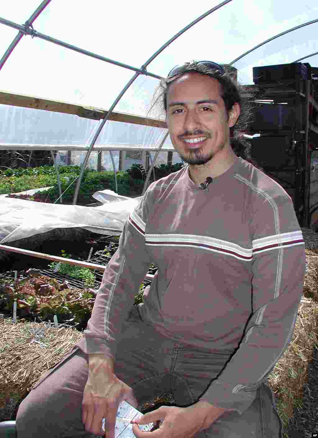 Farm manager Christian Melendez sits alongside incubating seedlings that tap into compost heat. (Rosanne Skirble/VOA)