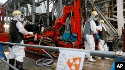 Para pekerja mengebor pipa ke dalam tanah yang digunakan untuk menciptakan dinding bawah tanah beku di PLTN Fukushima, timur laut Tokyo, Juli 2014. (AP/Kimimasa Mayama)