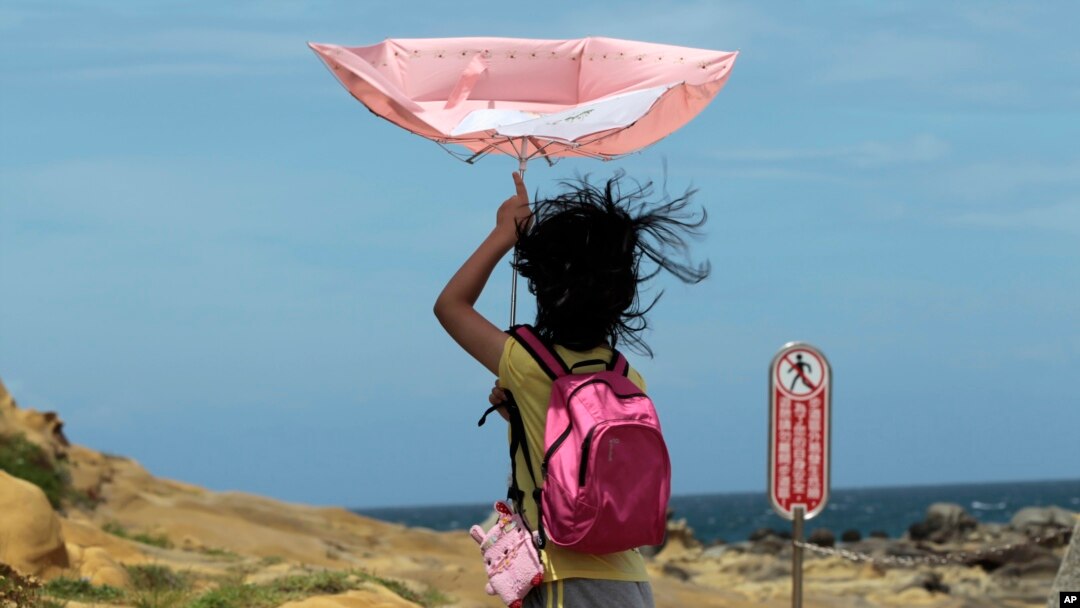 Seorang anak perempuan berusaha mengendalikan payungnya saat topan Matmo mendekati kawasan pantai di Keelung, Taiwan (22/7). (AP/Wally Santana)
