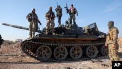 (FILE) Syrian opposition fighters stand atop a seized military armored vehicle on the outskirts of Hama, Syria, Tuesday, Dec. 3, 2024.