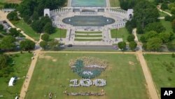 People on the National Mall in Washington, looking toward the World War II Memorial, Aug. 25, 2016, recreate a giant, living version of the National Park Service emblem, using brown, green and white umbrellas. 