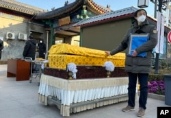 FILE - Family members in protective gear collect the cremated remains of their loved one bundled with yellow cloth at a crematorium in Beijing on Dec. 17, 2022. (AP Photo/Ng Han Guan, File)