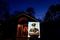 An image of veteran Roy Benson is projected onto the home of his daughter, Robin Benson Wilson, left, as she looks out a doorway with her husband, Donald, in Holland, Mass., May 13, 2020.