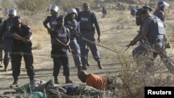 South African policemen give instructions to an injured miner after striking miners were shot outside a South African mine in Rustenburg, 100 km northwest of Johannesburg on August 16, 2012. 