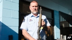 In this Aug. 31, 2019, photo. Police Senior Sgt. Braydon Lenihan poses holding a banned gun that has been bent by a hydraulic machine outside a temporary gun collection venue in Porirua, near Wellington, New Zealand. (AP photo/Nick Perry)