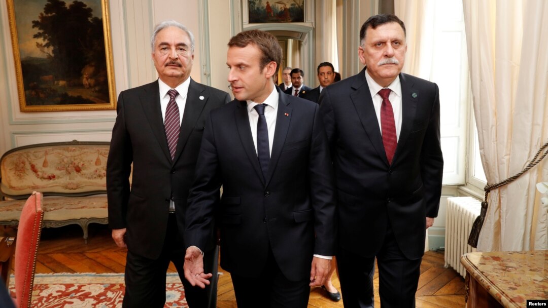 Presiden Perancis Emmanuel Macron (tengah) berjalan bersama PM LIbya Fayez al-Sarraj (kanan) dan Jenderal Khalifa Haftar sebelum pertemuan di Paris, Selasa (25/7). 