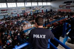 A policeman observes the scene as immigrants who arrived aboard a cargo ship from Turkey queue for meals in a basketball arena where they have been given temporary shelter in the town of Ierapetra, Crete, Nov. 28, 2014.