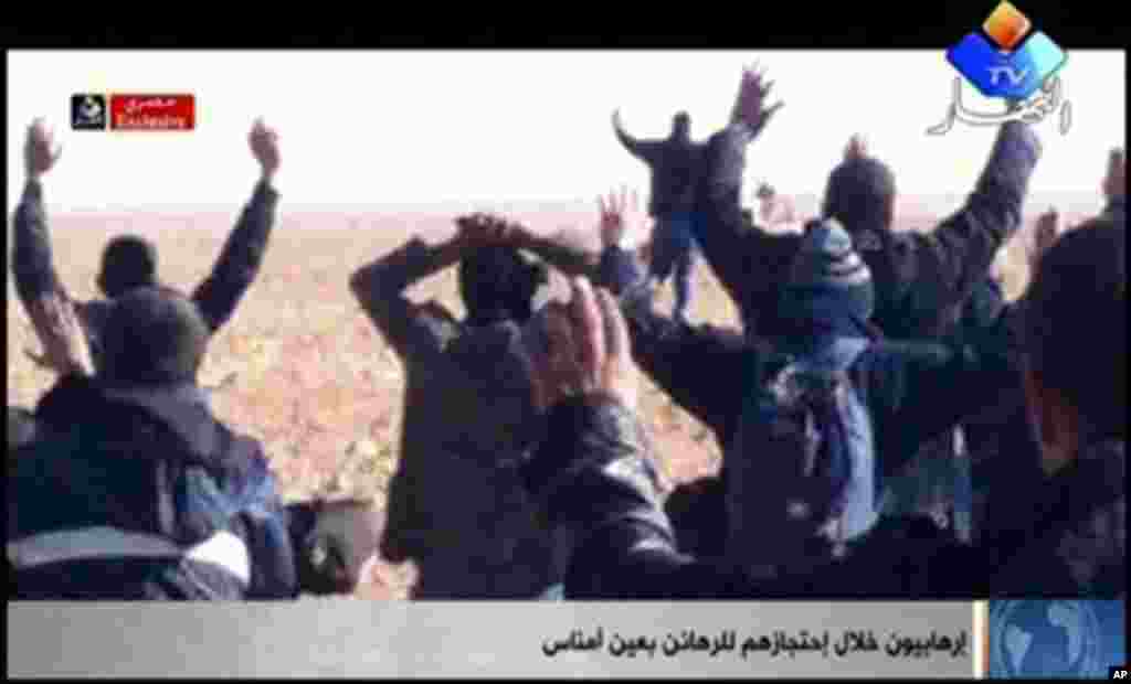 In this image made from video, a group of people believed to be hostages kneel in the sand with their hands in the air at an unknown location in Algeria. An Algerian security official says de-mining squads searching for explosives found &quot;numerous&quot; bodies Sunday, Jan. 20, 2012 at a gas refinery where Islamic militants took dozens of foreign workers hostage.