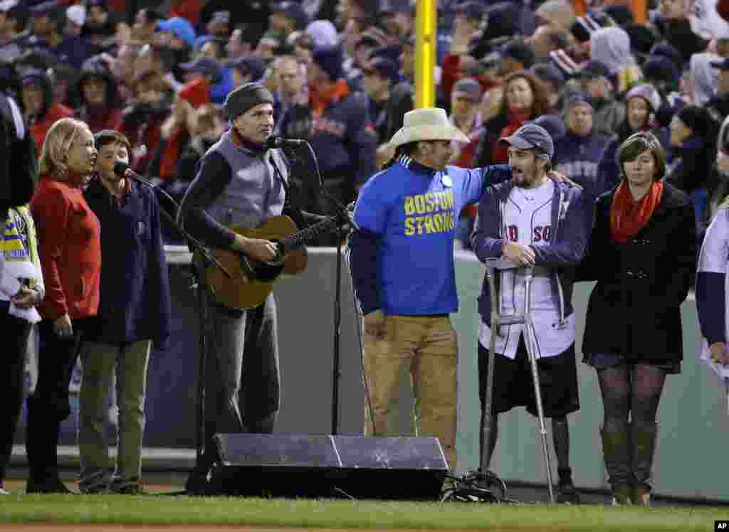 James Taylor sings "God Bless America" alongside Carlos Arredondo, center, and Boston Marathon bombing survivor Jeff Bauman, second from right, during the seventh inning stretch of Game 2 of baseball's World Series between the Boston Red Sox and the St. Louis Cardinals.