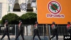 Police march past a billboard related to stopping the spread of the Covid-19 coronavirus as protesters gather for a demonstration against the military coup in Yangon on February 6, 2021. (Photo by YE AUNG THU / AFP)