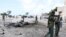 Somalian security forces walk past the remains of a car after it exploded outside Somali parliament building, Mogadishu, July 5, 2014.