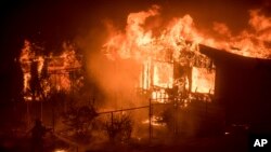 A firefighter sprays water as flames from a wildfire consume a residence near Oroville, Calif., on Sunday, July 9, 2017. Evening winds drove the fire through several neighborhoods leveling homes in its path.