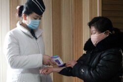 A staff member, left, of the Pongnam Noodle House checks the body temperature of a woman coming into its restaurant in Pyongyang, North Korea, Feb. 5, 2021.