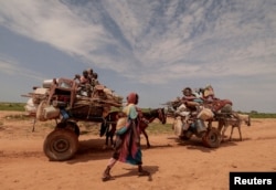 FILE - A Sudanese woman fleeing conflict in Sudan's Darfur region walks next to a trolley carrying her family's belongings as they cross the border between Sudan and Chad in Adre, Chad, August 2, 2023.