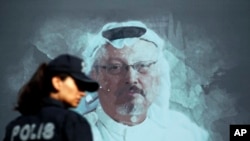 FILE —A Turkish police officer walks past a picture of slain Saudi journalist Jamal Khashoggi prior to a ceremony, near the Saudi Arabia consulate in Istanbul, Oct. 2, 2019.