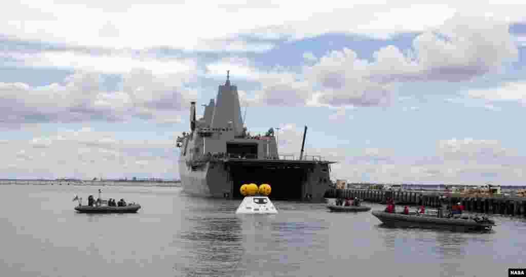 With the U.S. Navy&#39;s well deck ship USS Arlington stationed against its pier at Naval Station Norfolk in Virginia, divers in small boats approach a test version of NASA&#39;s Orion crew module during the stationary recovery test. The test is helping to ensure that when Orion returns from deep space missions and splashes down in the Pacific Ocean.